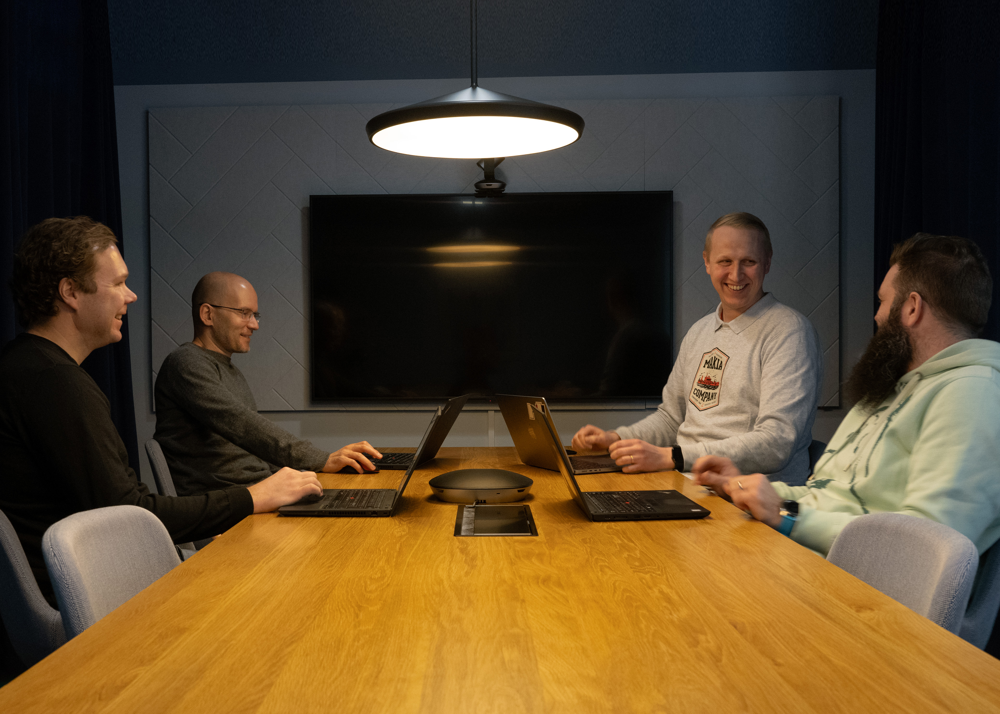 Four people with laptops gathered around a table in a meeting room