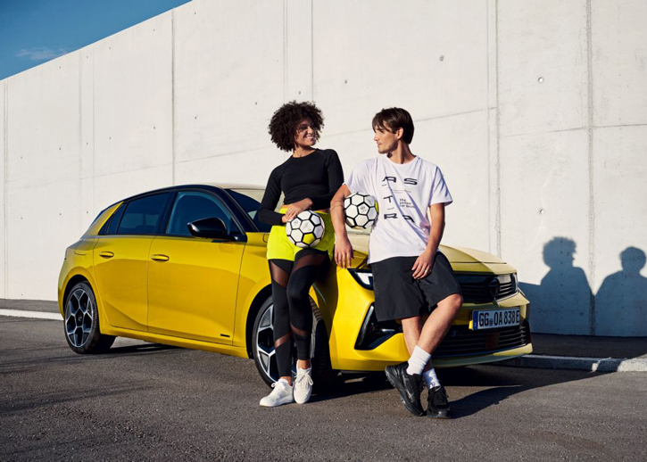 Two people holding footballs leaning against Opel car