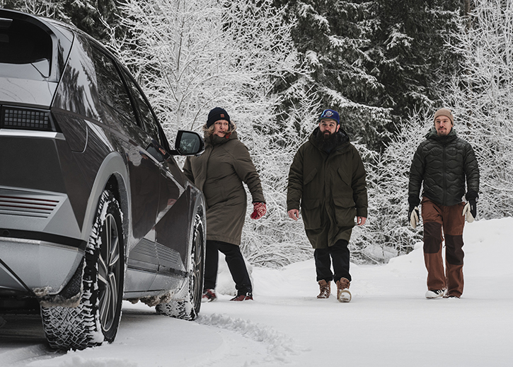 Three people walking towards a car in the snow 